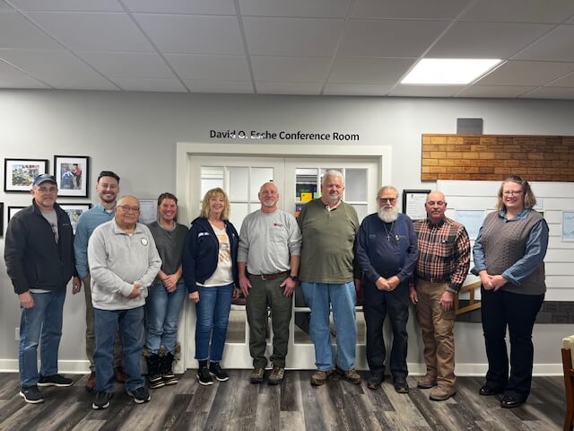 Ten Rebuilding Together Henry County board members standing together in front of the board room wall.
